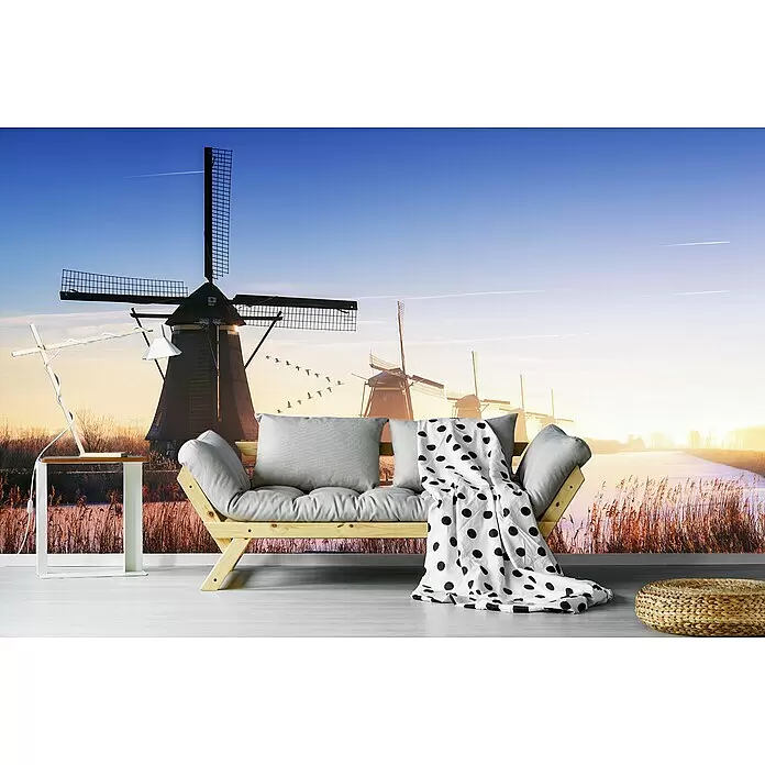 Papermoon Premium collection Fototapete Windmühle - B x H: 350 x 260 cm, Vlies - Ein helles Holzsofa mit grauen Kissen und einer weiß-gepunkteten Decke steht in einem Zimmer mit Windmühlen-Wandbild.