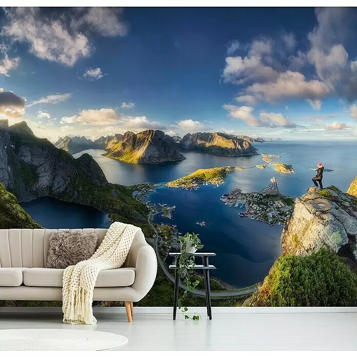 Papermoon Premium collection Fototapete Reinebringen Ansicht - B x H: 250 x 186 cm, Vlies - Wandbild mit Panoramablick auf eine dramatische Fjordlandschaft mit Bergen, Meer und Küstenstadt, hinter einem hellen Sofa angebracht.