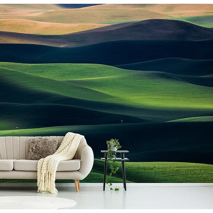 Papermoon Premium collection Fototapete Fließen - B x H: 350 x 260 cm, Vlies - Das gemütliche Wohnzimmer verfügt über eine beige Couch mit Kissen und Decke vor einer grünen Hügellandschaft als Wandbild.