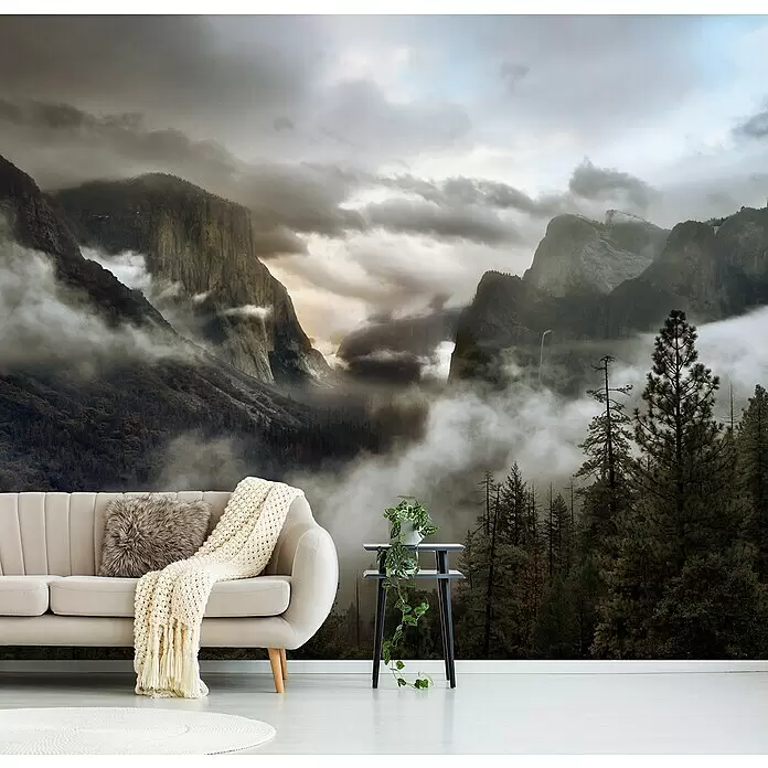 Papermoon Premium collection Fototapete Obertalmorgen - B x H: 450 x 280 cm, Vlies - Wandtapete mit nebeliger Gebirgslandschaft und Kiefern hinter einem Sofa und Beistelltisch in einem Zimmer.
