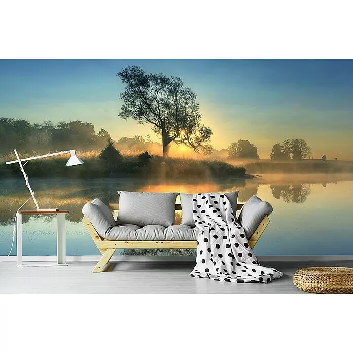 Papermoon Premium collection Fototapete Morgenreflexion - B x H: 500 x 280 cm, Vlies - Modernes helles Holzsofa mit grauen Kissen und gepunkteter Decke, dazu weiße Lampe auf Beistelltisch und geflochtener Hocker vor Naturwandbild.