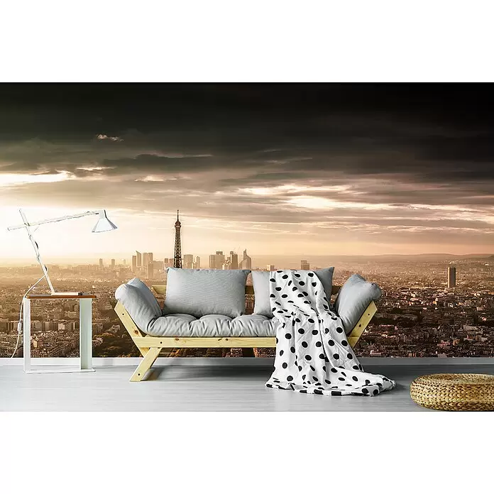 Papermoon Premium collection Fototapete Paris-Pracht - B x H: 400 x 260 cm, Vlies - Helles Holzsofa mit grauen Kissen und gepunkteter Decke, das eine gemütliche Sitzecke mit Blick auf eine Stadt bei Sonnenuntergang bildet.