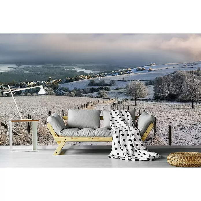 Papermoon Premium collection Fototapete Schneewanderung - B x H: 300 x 223 cm, Vlies - Helles Holzsofa mit grauen Kissen und weißer Tupfendecke, in einem Raum mit einer Winterlandschafts-Wandmalerei.