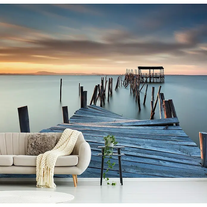 Papermoon Premium collection Fototapete Zusammengebrochen - B x H: 400 x 260 cm, Vlies - Eine Inneneinrichtung mit einer Fototapete, die einen alten Holzsteg zeigt, der ins ruhige Wasser führt, ergänzt durch ein stilvolles Sofa und Beistelltisch.