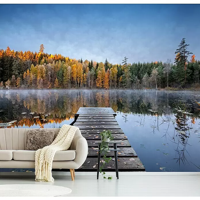 Papermoon Premium collection Fototapete Herbststeg - B x H: 300 x 223 cm, Vlies - Ein cremefarbenes Sofa mit Decke und ein Beistelltisch mit Topfpflanze vor einem Natur-Wandgemälde.