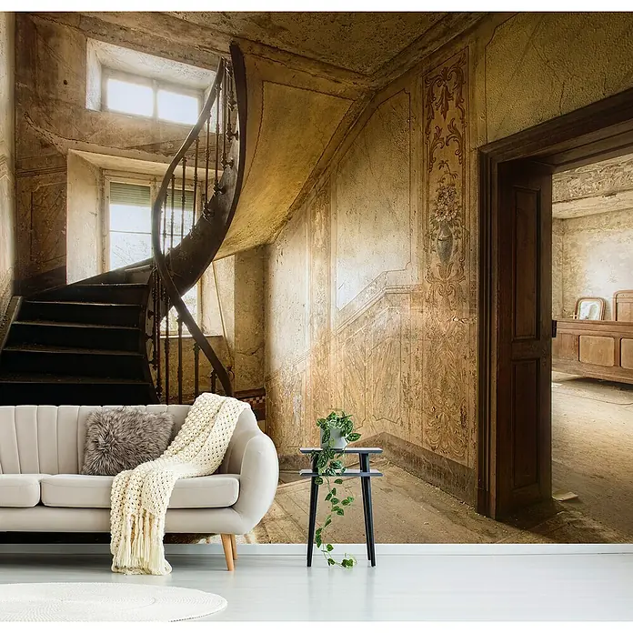 Papermoon Premium collection Fototapete Antiker Flur - B x H: 250 x 186 cm, Vlies - Ein stilvolles, cremefarbenes Sofa mit Kissen und Decke, kombiniert mit einem Beistelltisch und einer Pflanze, vor einer historischen Treppe.