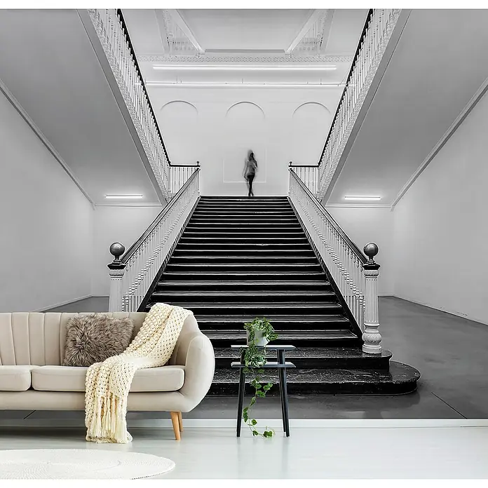 Papermoon Premium collection Fototapete Tabakalera - B x H: 450 x 280 cm, Vlies - Beigefarbenes Sofa mit Zierkissen und Überwurf vor einer großen Treppe. Ein dekorativer Beistelltisch mit Pflanze ergänzt das Ensemble.