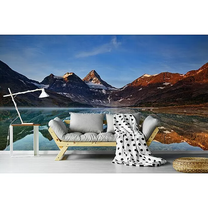 Papermoon Premium collection Fototapete Magog Lake - B x H: 300 x 223 cm, Vlies - Helles Holzsofa, graue Kissen, weiße gepunktete Decke, in einem Raum mit Bergsee-Wandbild.