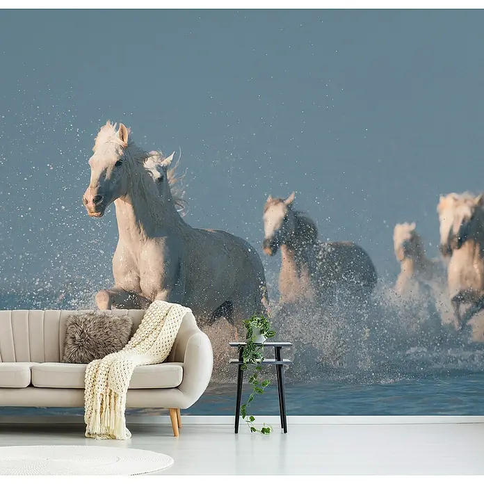 Papermoon Premium collection Fototapete Angels von Camargue - B x H: 500 x 280 cm, Vlies - Elegante Wohnraumgestaltung mit einer Tapete, die eine Herde weißer Pferde in Bewegung zeigt, ergänzt durch ein stilvolles Sofa und einen Beistelltisch.