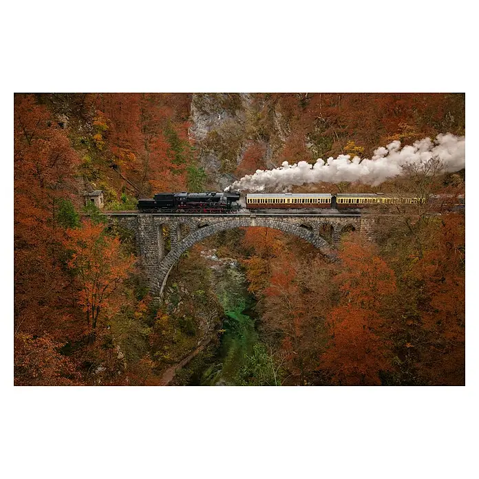 Papermoon Premium collection Fototapete Museumszug - B x H: 500 x 280 cm, Vlies - Eine Dampflokomotive zieht über eine Steinbrücke, umgeben von herbstlichen Wäldern.
