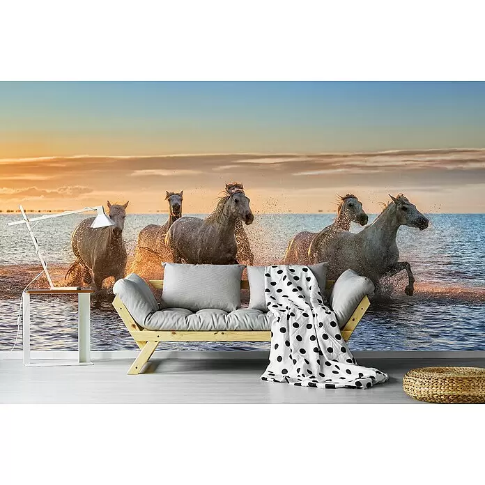 Papermoon Premium collection Fototapete Camargue-Pferde II - B x H: 250 x 186 cm, Vlies - Holzsofa mit grauen Kissen und gepunkteter Decke, ein weißer Beistelltisch mit Lampe und ein geflochtener Ottoman in einem Wohnraum.