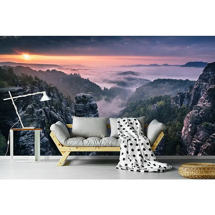 Papermoon Premium collection Fototapete Sonnenaufgang Felsen III - B x H: 350 x 260 cm, Vlies - Foto eines Wohnzimmers mit einem Sofa mit Kissen und einer Decke mit Punkten vor einer malerischen Landschaftstapete mit einem Sonnenaufgang.