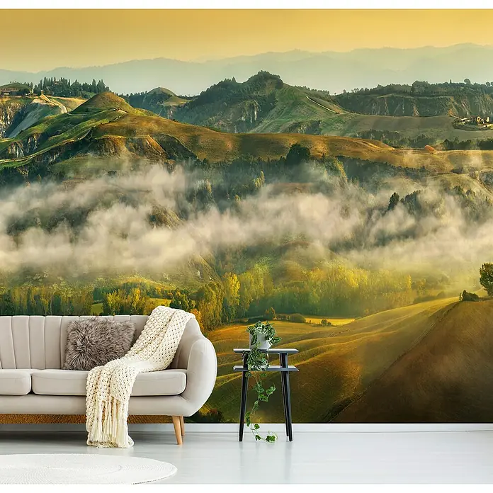 Papermoon Premium collection Fototapete Herbst - B x H: 250 x 186 cm, Vlies - Beige Couch mit Kissen und Decke vor einer Fototapete mit einer Landschaft. Eine Pflanze steht auf einem kleinen Tisch daneben.