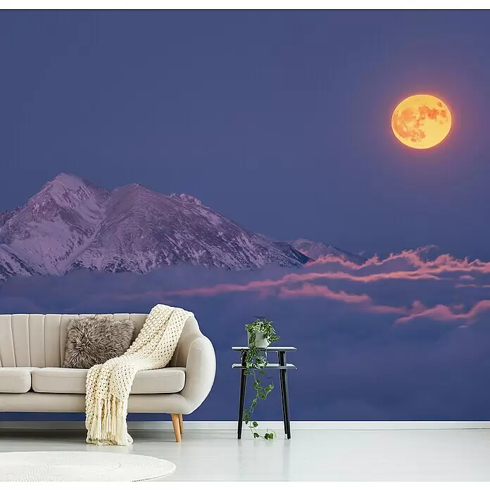 Papermoon Premium collection Fototapete Mond über den Wolken - B x H: 350 x 260 cm, Vlies - Wandtapete mit schneebedeckten Bergen unter einem großen orangefarbenen Vollmond und lila Himmel, an einer Wohnzimmerwand hinter einem beigen Sofa.