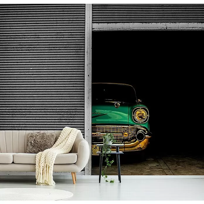 Papermoon Premium collection Fototapete Versteckte Schönheit - B x H: 350 x 260 cm, Vlies - Wandbild mit der Front eines grünen Oldtimers, der aus einer dunklen Garage fährt, hinter einem beigefarbenen Sofa und Beistelltisch.