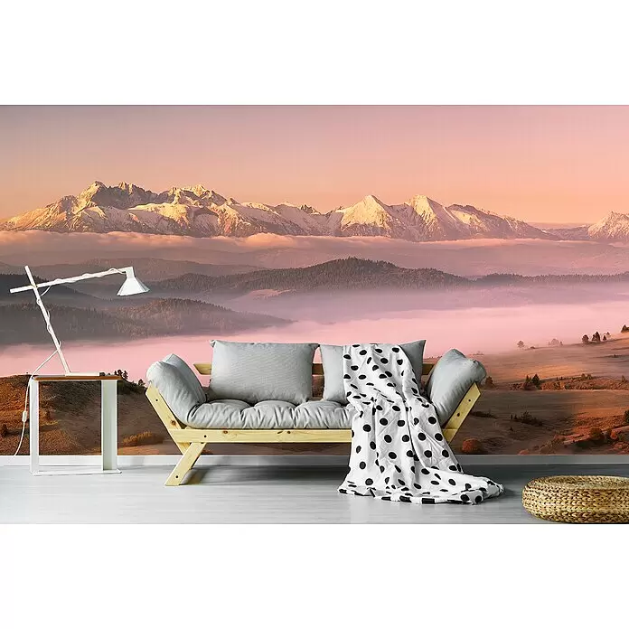 Papermoon Premium collection Fototapete Nebel Tatra - B x H: 250 x 186 cm, Vlies - Sofa mit Holzrahmen, hellgrauen Kissen und Tupfendecke, in einem Raum mit Bergwandbild, Beistelltisch und Flechtpouf.