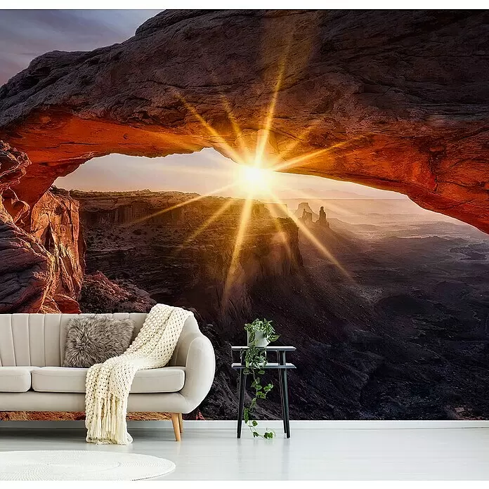 Papermoon Premium collection Fototapete Mesa Arch - B x H: 400 x 260 cm, Vlies - Wandbild mit natürlicher Felsbrücke bei Sonnenaufgang mit strahlenden Sonnenstrahlen, hinter beigefarbenem Sofa und Beistelltisch angebracht.