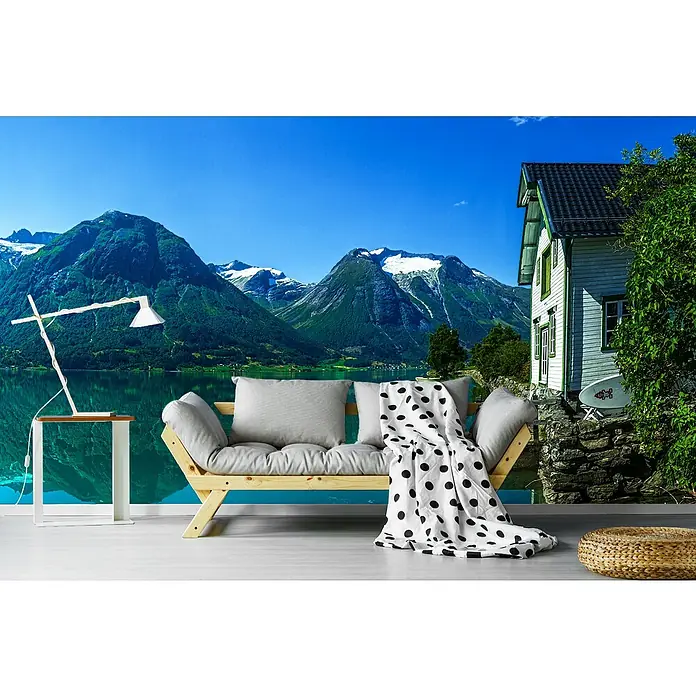 Papermoon Premium collection Fototapete Haus Gletschersee - B x H: 450 x 280 cm, Vlies - Wohnzimmer mit einem stilvollen Sofa mit Kissen und einer Decke im Punktmuster, ergänzt durch eine moderne Lampe und einen Hocker.