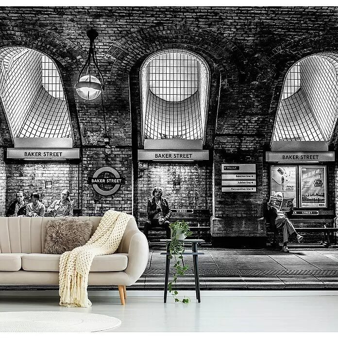 Papermoon Premium collection Fototapete Bäckerstraße - B x H: 250 x 186 cm, Vlies - Beiges Sofa mit Kunstfellkissen und Strickdecke, vor einer schwarz-weißen U-Bahn-Mural.