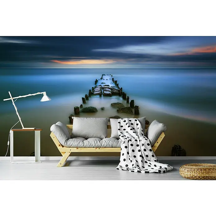 Papermoon Premium collection Fototapete Baltisch - B x H: 350 x 260 cm, Vlies - Gemütliches Wohnzimmer mit einer hölzernen Couch, grauen Kissen, einer Decke mit Punkten und einer Stehlampe neben einem kleinen Tisch.