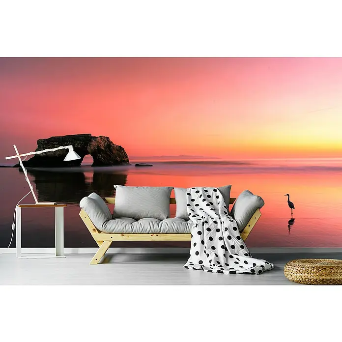 Papermoon Premium collection Fototapete Sonnenuntergang Naturbrücke - B x H: 400 x 260 cm, Vlies - Gemütliches Zimmer mit einem hellen Holzsofa, grauen Kissen und einer Decke mit Tupfenmuster vor einer beruhigenden Strandszene.