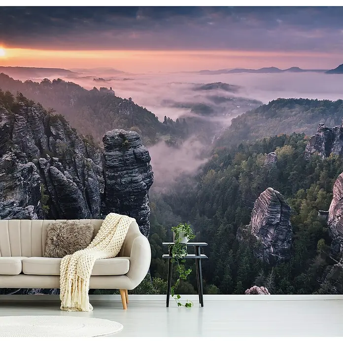 Papermoon Premium collection Fototapete Sonnenaufgang Felsen III - B x H: 350 x 260 cm, Vlies - Ein gemütliches Wohnzimmer mit einer Fototapete, die eine atemberaubende Berglandschaft in mystischem Nebel zeigt. Stilvolle Möbel ergänzen die friedliche Atmosphäre.