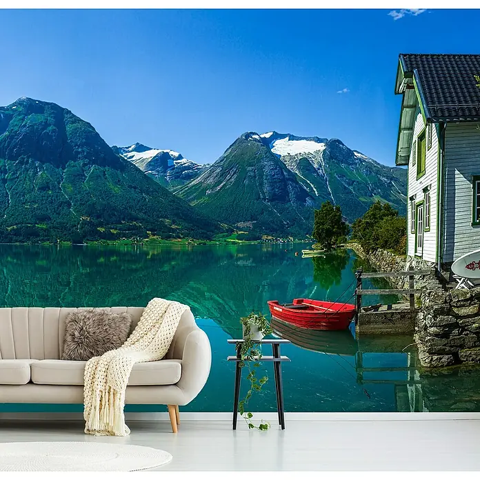 Papermoon Premium collection Fototapete Haus Gletschersee - B x H: 450 x 280 cm, Vlies - Wandbild mit einem Sofa im Vordergrund und einer malerischen Landschaft mit See und Bergen im Hintergrund.