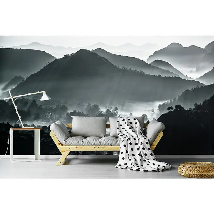 Papermoon Premium collection Fototapete Nebliges Meer von Wolken - B x H: 350 x 260 cm, Vlies - Wandbild mit Berglandschaft hinter einem hellen Holzsofa mit Kissen und einer gepunkteten Decke, ergänzt durch Beistelltisch und Hocker.