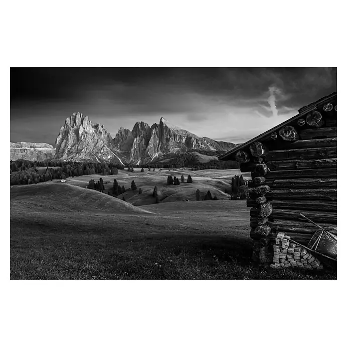 Papermoon Premium collection Fototapete Berghütte - B x H: 500 x 280 cm, Vlies - Das Foto zeigt eine urige Berghütte vor einer dramatischen Bergkulisse in Schwarzweiß, die traditionelle Architektur und Natur vereint.