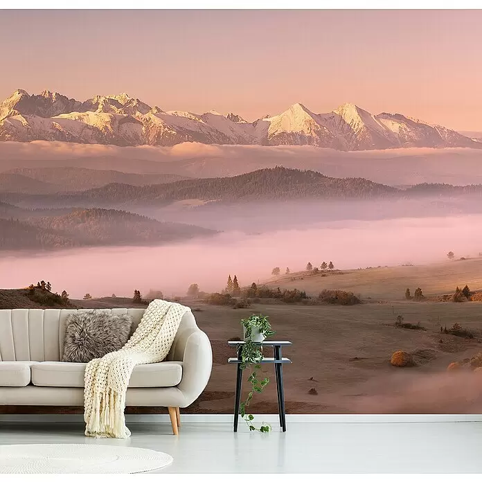Papermoon Premium collection Fototapete Nebel Tatra - B x H: 250 x 186 cm, Vlies - Wandbild mit Berglandschaft, schneebedeckten Gipfeln und nebligen Tälern bei Sonnenauf-/untergang, hinter einem hellen Sofa.