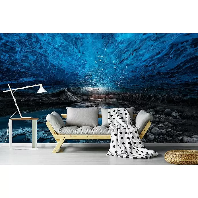 Papermoon Premium collection Fototapete Eishöhle - B x H: 400 x 260 cm, Vlies - Ein helles Holzsofa mit grauen Kissen und einer gepunkteten Decke, in einem Raum mit einem Eishöhlen-Wandbild.