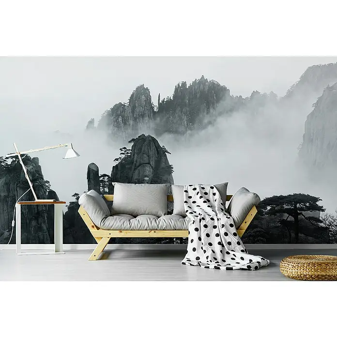 Papermoon Premium collection Fototapete Huangshan - B x H: 450 x 280 cm, Vlies - Ein stilvolles Interieur mit einem hellen Holzsofa, Kissen und einer Decke mit Punktmuster vor einer Bergkulisse als Wandbild.