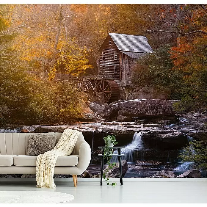 Papermoon Premium collection Fototapete Die Mühle - B x H: 250 x 186 cm, Vlies - Wandbild mit herbstlicher Waldszene, Wassermühle und Wasserfall, in einem Wohnzimmer hinter einem hellen Sofa.