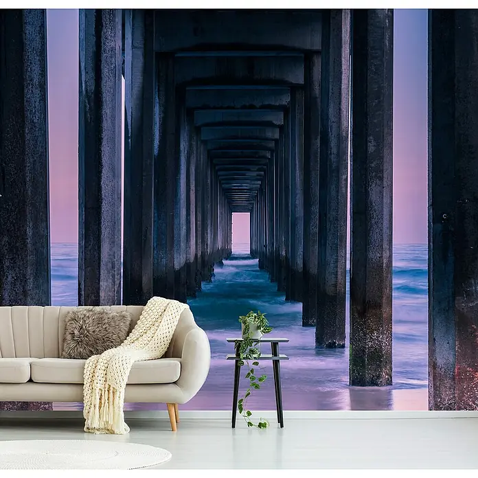 Papermoon Premium collection Fototapete Säulen zum Meer - B x H: 250 x 186 cm, Vlies - Wohnzimmer mit beigem Sofa, Beistelltisch und Fototapete einer Seebrücke bei Sonnenuntergang. Die Tapete ist ein echter Blickfang!