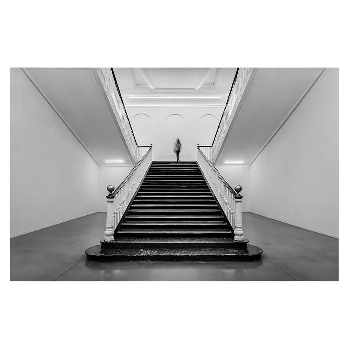 Papermoon Premium collection Fototapete Tabakalera - B x H: 450 x 280 cm, Vlies - Schwarz-Weiß-Foto einer Treppe in einem Gebäude, mit einer verschwommenen Person, die die Stufen hinaufsteigt, was eine dynamische Atmosphäre erzeugt.