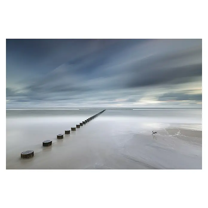 Papermoon Premium collection Fototapete Ebbe - B x H: 200 x 149 cm, Vlies - Malerische Küstenaufnahme mit einer Reihe von Holzpfählen, die ins Meer führen, unter einem bewegten, dramatischen Himmel.