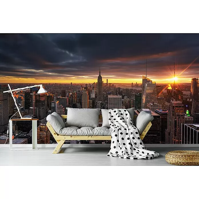 Papermoon Premium collection Fototapete Oben - B x H: 300 x 223 cm, Vlies - Ein Holzfuton mit grauen Kissen und gepunkteter Decke, ein weißer Beistelltisch mit Lampe und ein geflochtener Hocker in einem Zimmer mit Stadtblick.