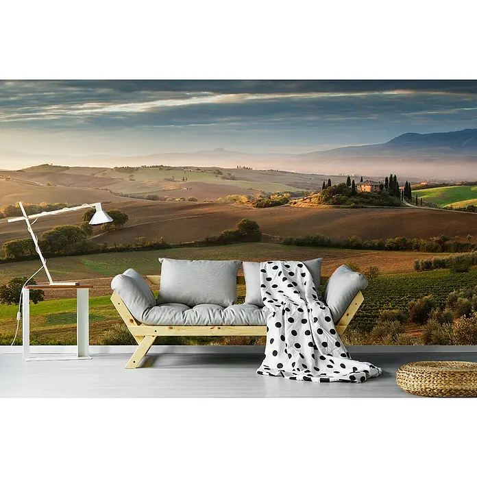 Papermoon Premium collection Fototapete Märchenliches Morgengrauen - B x H: 350 x 260 cm, Vlies - Eine stilvolle Inneneinrichtung mit einem Wandbild einer toskanischen Landschaft, einem modernen Sofa und einer Lampe.