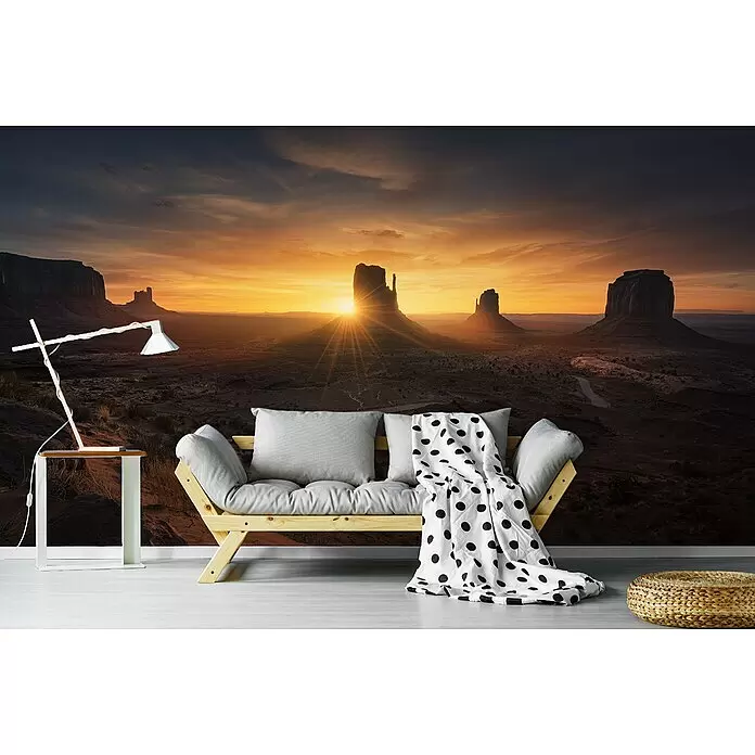 Papermoon Premium collection Fototapete Denkmal Sonnenaufgang - B x H: 200 x 149 cm, Vlies - Modernes Holzsofa mit hellgrauen Kissen, gepunkteter Decke, Beistelltisch mit Lampe und geflochtenem Pouf in einem Raum mit Wüstenmural.