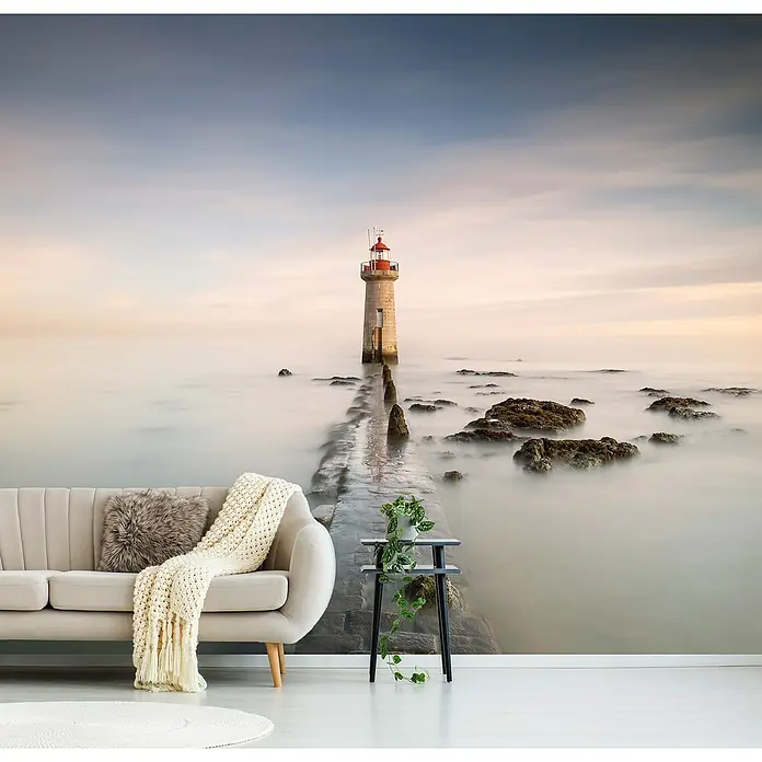 Papermoon Premium collection Fototapete Leuchtturm - B x H: 250 x 186 cm, Vlies - Stimmungsvolles Wohnzimmer mit einer Fototapete, die einen Leuchtturm im Nebel zeigt, ergänzt durch ein beiges Sofa und einen Beistelltisch.