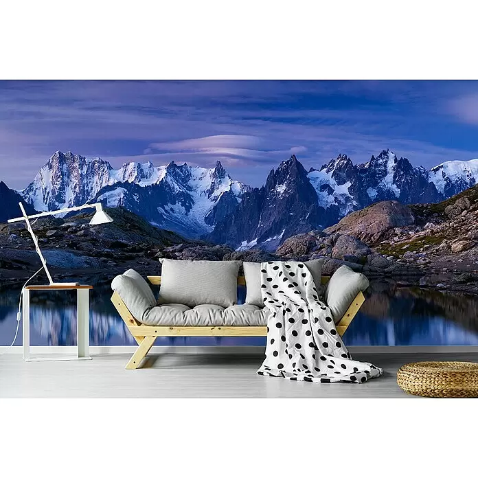Papermoon Premium collection Fototapete Träume Morgengrauen - B x H: 450 x 280 cm, Vlies - Holzsofa mit grauen Kissen und gepunkteter Decke, Beistelltisch mit Lampe, geflochtener Ottoman in Raum mit Bergwandbild.