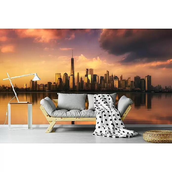 Papermoon Premium collection Fototapete Skyscraperview I - B x H: 400 x 260 cm, Vlies - Holzsofa mit grauen Kissen und gepunkteter Decke, weißer Beistelltisch mit Lampe und geflochtenem Pouf in einem Raum mit Stadtblick.