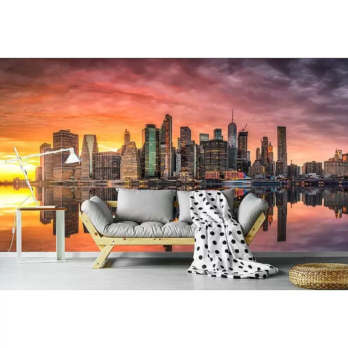 Papermoon Premium collection Fototapete New York Glühen I - B x H: 250 x 186 cm, Vlies - Helles Holz-Futonsofa mit grauen Kissen und einer gepunkteten Decke, in einem Raum mit Stadtkulissen-Wandbild.