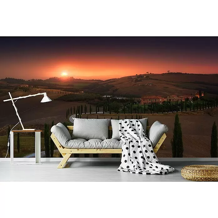Papermoon Premium collection Fototapete Toskana - B x H: 250 x 186 cm, Vlies - Holzsofa mit grauen Kissen und gepunkteter Decke, weiße Lampe auf Tisch und geflochtener Pouf in Raum mit Landschaftswandbild.