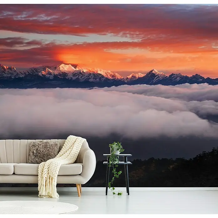 Papermoon Premium collection Fototapete Die Berggötter - B x H: 450 x 280 cm, Vlies - Wohnzimmer mit cremefarbenem Sofa, Decke und Kissen vor einer Tapete mit Berglandschaft bei Sonnenuntergang.