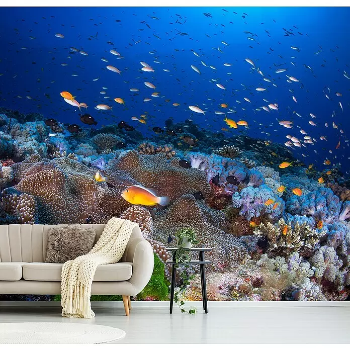 Papermoon Premium collection Fototapete Anemon und Anthias - B x H: 400 x 260 cm, Vlies - Lebendiges Unterwasser-Korallenriff-Wandbild mit Fischen, hinter einem hellbeigen Sofa.