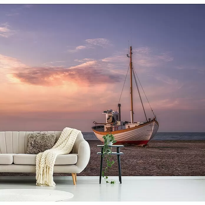 Papermoon Premium collection Fototapete Jammerbugten - B x H: 400 x 260 cm, Vlies - Beiges Sofa mit grauem Kunstfellkissen und cremefarbener Strickdecke, vor einer großen Boots-Sonnenuntergangs-Wandtapete.