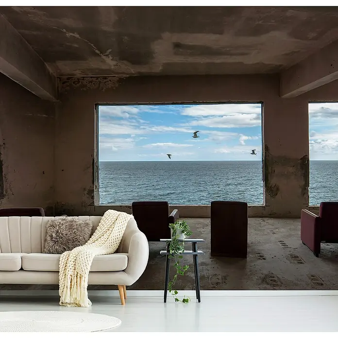 Papermoon Premium collection Fototapete Kino - B x H: 450 x 280 cm, Vlies - Elegantes cremefarbenes Sofa mit flauschigem Kissen und Strickdecke in einem Raum mit Meerblick. Moderne Möbel für stilvolles Wohnen.