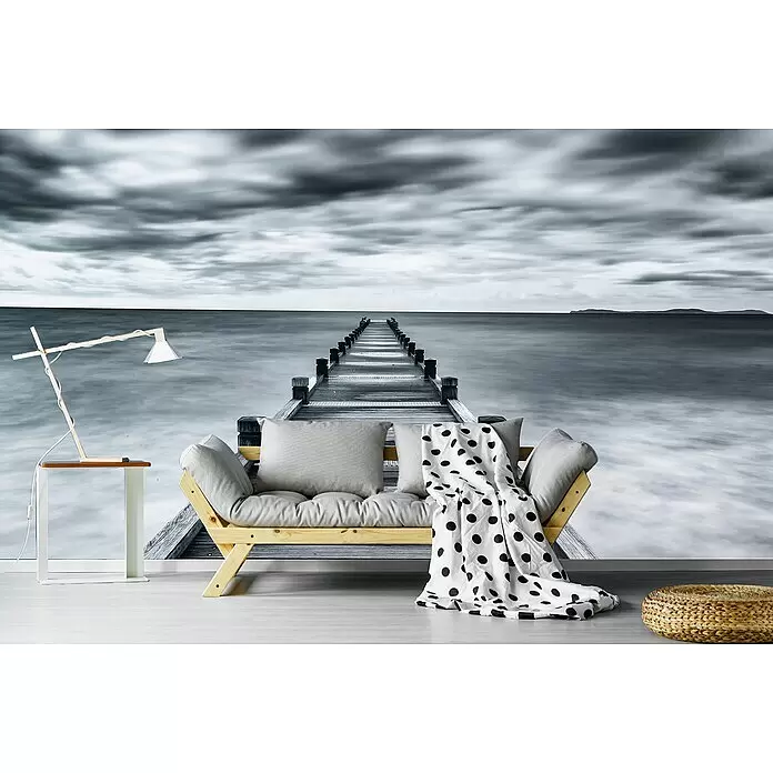 Papermoon Premium collection Fototapete Beinbar - B x H: 200 x 149 cm, Vlies - Helles Holzsofa mit grauen Kissen, Tupfendecke, Beistelltisch, Lampe und Flechtpouf vor Meer-Pier-Wandbild.