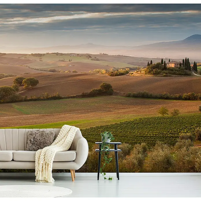 Papermoon Premium collection Fototapete Märchenliches Morgengrauen - B x H: 350 x 260 cm, Vlies - Das Foto zeigt ein helles Wohnzimmer mit einem Sofa und einem Tisch, vor einer Fototapete mit toskanischer Landschaft.